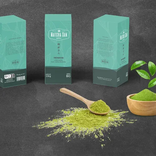 mock up de boites de thé Macha San. 3 boites sont posées sur une table noir. Il y a un tas de thé vert ainsi qu'une cuillère et un bol en bois.